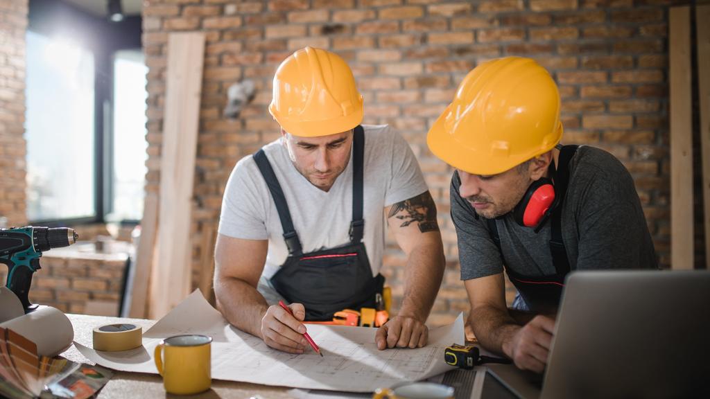 Construction workers cooperating while analyzing housing project in apartment.