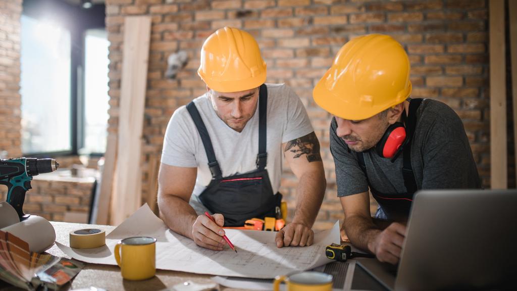 Construction workers cooperating while analyzing housing project in apartment.