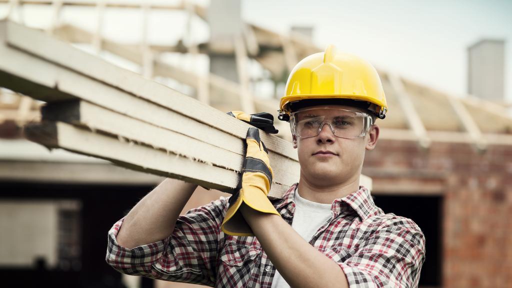 Young construction worker carrying wood boards