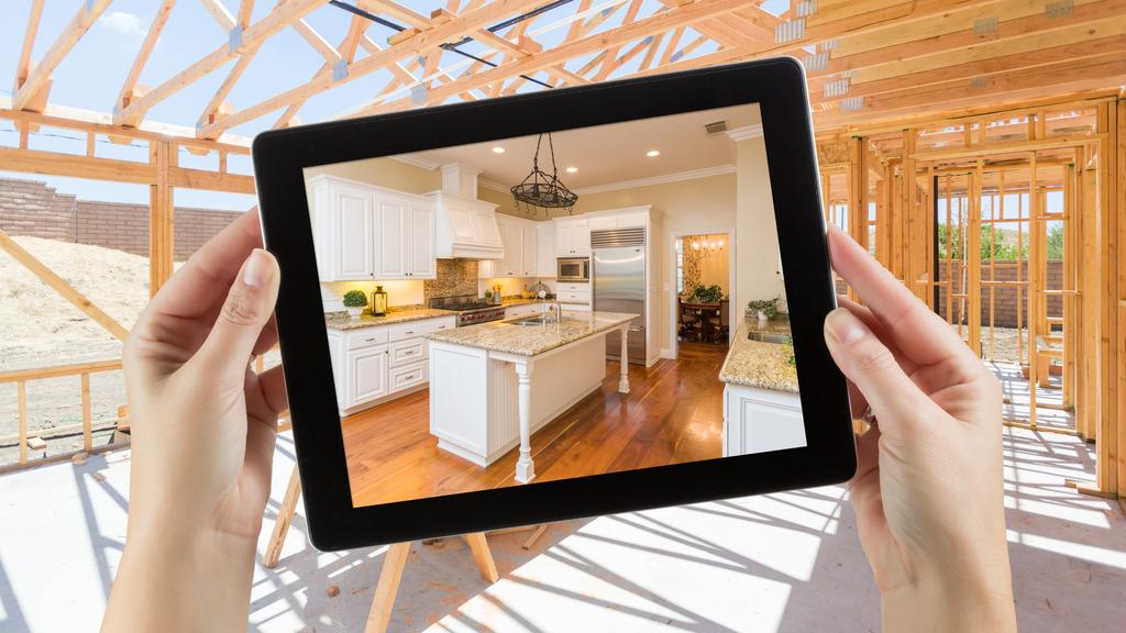 Female Hands Holding Computer Tablet with Finished Kitchen on Screen, Construction Framing Behind.