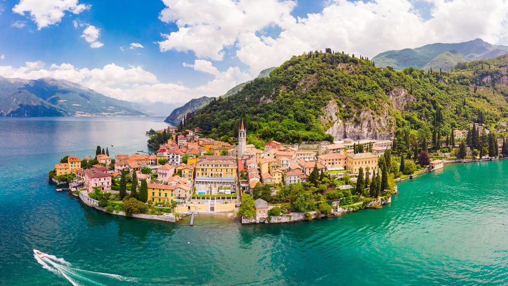 Beautifull aerial panoramic view from the drone to the Varenna - famous old Italy town on bank of Como lake. High top view to Water landscape with green hills, mountains and city in sunny summer day.